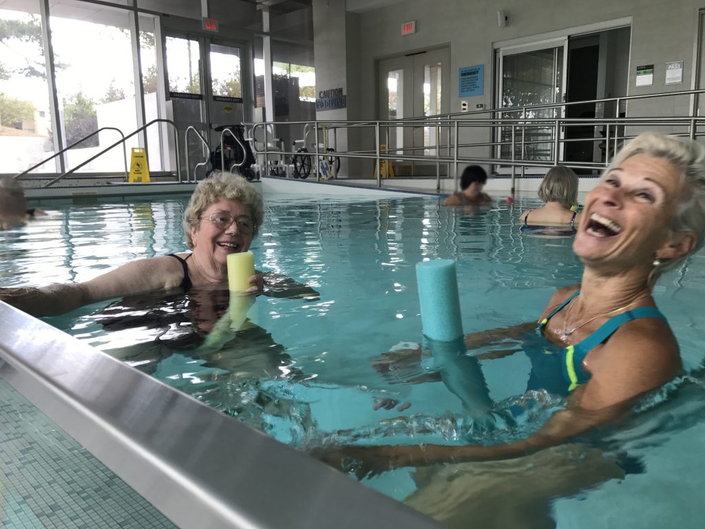 A participant in a pool fitness class and the instructor in the pool