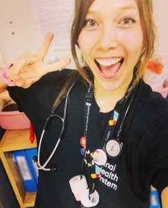 Woman in black Sinai Health System t-shirt wearing a stethoscope and making the peace sign with her hand