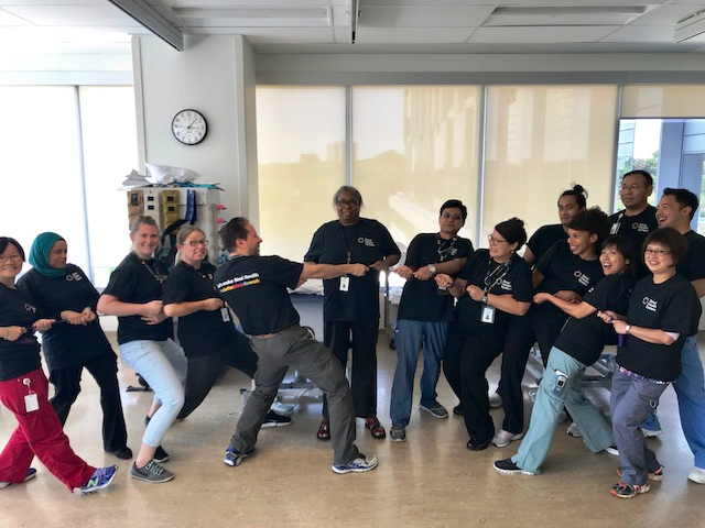 employees from a unit wearing black sinai health system t-shirts pretending to play tug of war