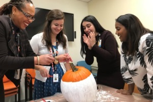 A group of four employees work on painting and decorating a pumpkin