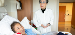 a patient of Chinese descent in hospital bed, family member standing next to them